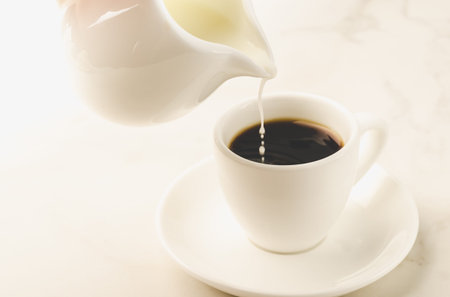 milk is added to coffee white cup/milk is added to coffee cup on a white background. Selective focusの写真素材