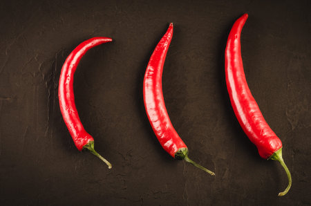 Three red Chile pepper on a dark background/Three red hot Chile pepper on a dark stone background....