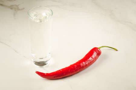 shot of vodka and red hot chili pepper on the bar/shot of vodka and red hot chili pepper on a white marble background. Selective focusの写真素材