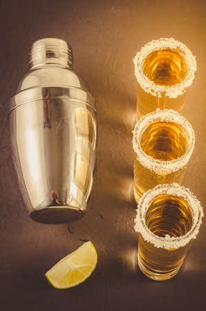 Mexican alcoholic drink with lime and shaker/traditional Mexican strong alcoholic drink with lime and shaker on a dark stone background. Top view. Tonedの写真素材