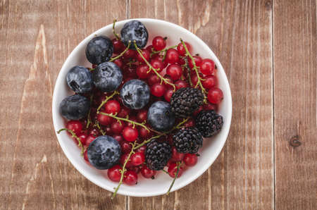 abundance of berries in a white bowl/ abundance of berries in a white bowl on a wooden background. Top viewの写真素材