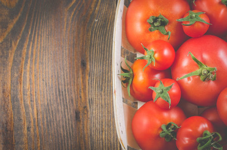 tomatoes in a wattled basket on a wooden background/tomatoes in a wattled container on a dark wooden background, top view and copy spaceの写真素材