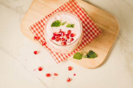 Yogurt. Yogurt with garnet and mint in glass on a wooden tray and the scattered pomegranate seeds on...