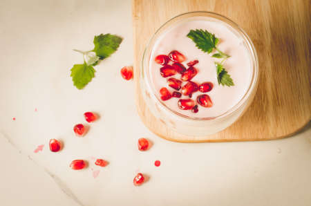 Yogurt. Yogurt with garnet and mint in glass on a wooden tray and the scattered pomegranate seeds on a white table. Top view. Sweet dessertの写真素材