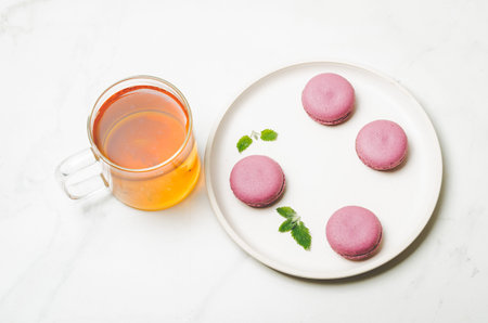 sweet macaroons or macaron with mint leaves in a white bowl and tea in a glass on a white background, top view, french dessertの写真素材