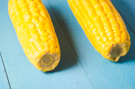 Two ears of boiled appetizing corn on a blue table. Healthy food. Selective focus