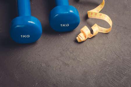 Blue dumbbells and yellow centimeter/sports concept: Blue dumbbells and yellow centimeter on a dark background. Copy spaceの写真素材