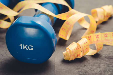 Blue dumbbells and yellow centimeter/fitness concept with blue dumbbells and yellow centimeter on a dark background. Close upの写真素材