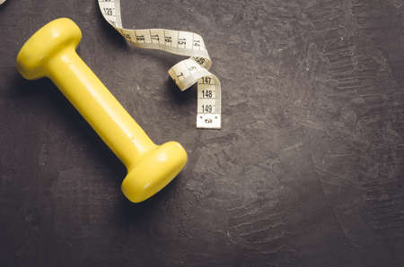 fitness equipment on a dark background/fitness equipment with yellow dumbbell and measuring tape. Top view and copy spaceの写真素材