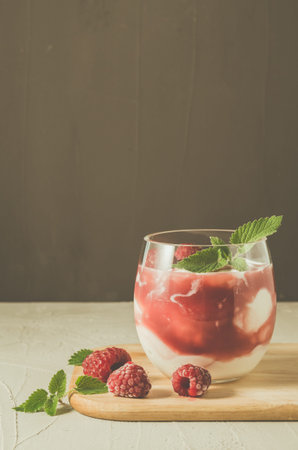 glass of raspberry yogurt with mint/yogurt with raspberry and mint on a wooden tray, closeup. Healthy breakfast. Selective focusの写真素材