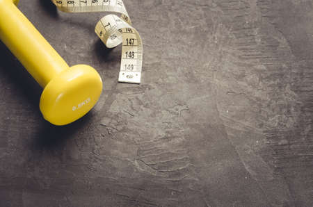 yellow dumbbell and measuring tape/fitness concept with yellow dumbbell and measuring tape on a dark background. Top view and copy spaceの写真素材