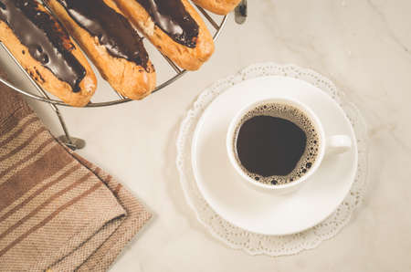 breakfast with eclairs with chocolate and a coffee cup/breakfast with eclairs with chocolate and a coffee cup on a white marble background, top viewの写真素材