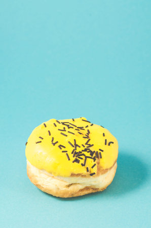 yellow donut isolated on blue background/Donut in yellow glaze decorated with dark chocolate sticks on blue background.の写真素材