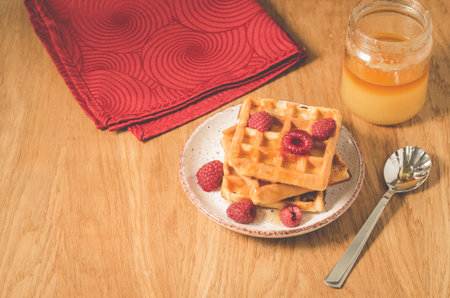 Waffles With raspberry in plate on a red napkin/waffles with raspberry in plate on a red napkin, and jar of honey on a wooden tableの写真素材
