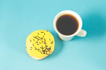 Donut and coffe cup on blue background/Donut in yellow glaze decorated with dark chocolate sticks and coffe cup on blue background. Top viewの写真素材