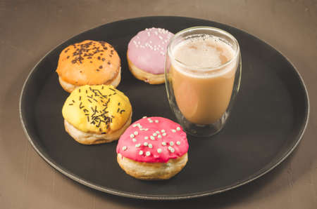 donuts in glazes and a glass of a cappuccino/donuts in glazes and a glass of a cappuccino on a black trayの写真素材