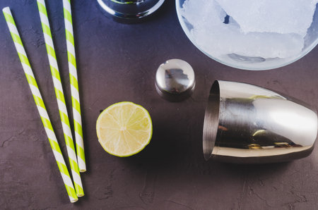 Cocktail shaker, lime, ice and straws/Cocktail shaker, lime, ice and straws on a dark background....