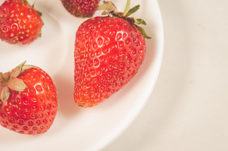 red strawberry berries in a white bowl/red strawberry berries in a white bowl on a white table...