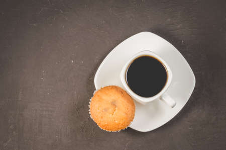 coffee break. White cup of the hot black coffee and cupcake on a dark background copy space, top view. Breakfast conceptの写真素材