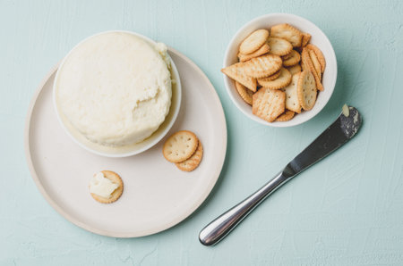 Cheese and cracker in a white bowl with a knife on a light green