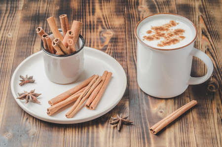 Eggnog. Traditional christmas cocktail in a mug and cinnamon sticks and anise on a white bowl on a woodenの写真素材