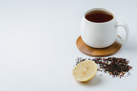 Fruit tea in a white mug on a bamboo support, lemon and dried tea isolated on white