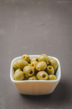 Green olives in a white ceramic bowl on a darkの写真素材