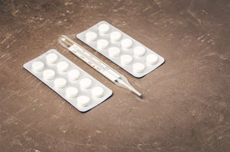 Two pills packages and thermometer on black background/ Packages of pills and thermometer are placed on a black background. Top view and copyspaceの写真素材