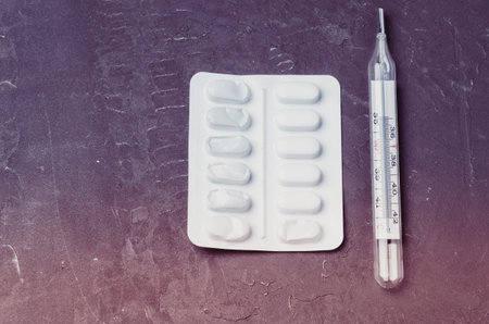 Two pills packages and thermometer on black background/ Packages of pills and thermometer are placed...