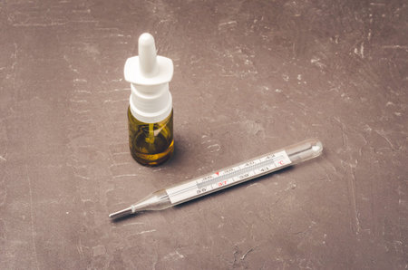 Drug spray bottle and thermometer on black background/Drug spray bottle and thermometer are placed...