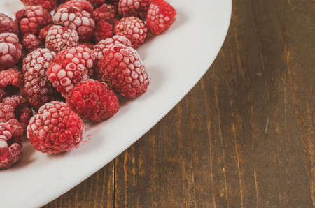 frozen raspberry on a dish/frozen raspberry on a white dish and wooden table, top view and copy spaceの写真素材