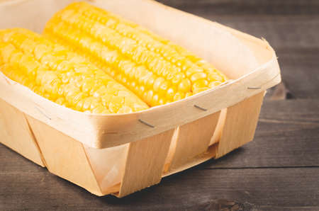 Corn. Appetizing boiled corn in a small basket on a wooden table. の写真素材