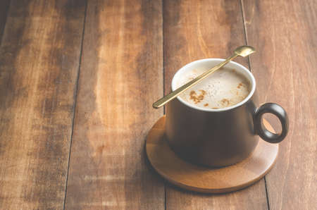 black mug of a cappuccino with a spoon in a wooden support, on a wooden table. Copy spaceの写真素材