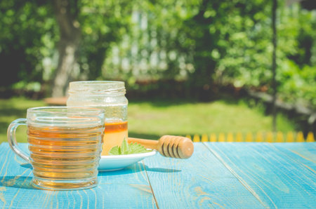 glass cup of tea with a honey jar on a blue wooden table in a summer garden. Copy spaceの写真素材