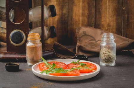 Salad. The sliced tomato with arugula in a white bowl, with spices against a dark background.の写真素材