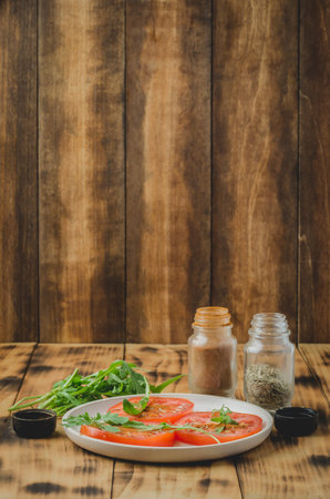 sliced tomatoes and arugula spices salad. In a white bowl on a wooden background. Selective focusの写真素材