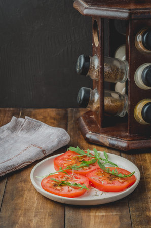 Salad. The sliced tomato with arugula in a white bowl, with spices against a dark background.の写真素材