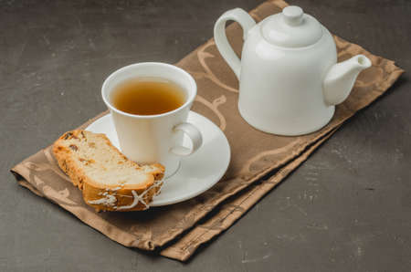 White tea cup and teapot with a pastries piece on dark stone table. Breakfast.の写真素材
