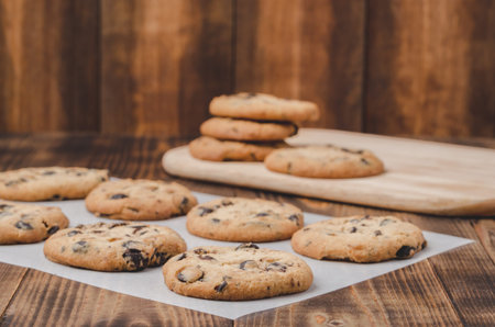 Cookies with chocolate filling on baking paper and wooden table/Cookies with chocolate filling on...