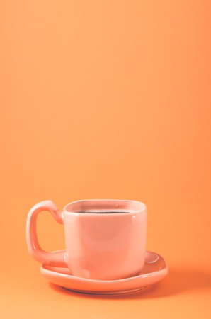pink cup with a saucer on a orange background/pink cup of coffee on a orange background, close upの写真素材