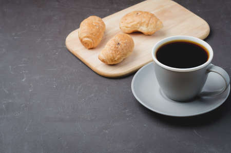 Grey cup with black coffee and wooden tray with croissants on dark table. Copyspace. Coffee break.の写真素材