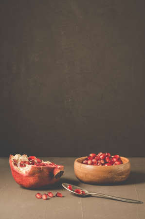 Pomegranate fruit and grains in a wooden bowl and a spoon/Pomegranate fruit and grains in a wooden bowl and a spoon against a dark background with copy spaceの写真素材