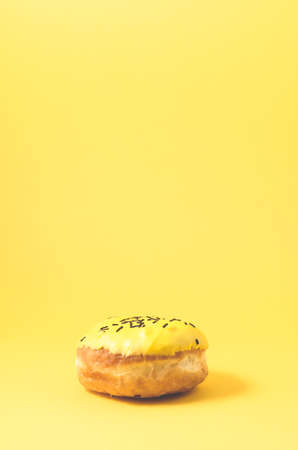 yellow donut isolated on yellow background/Donut in yellow glaze decorated with dark chocolate sticks on yellow background with copy spaceの写真素材