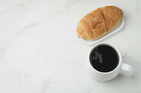 White mug with black coffee and croissant on white stone table. Top view and copyspace. Coffee break.の写真素材
