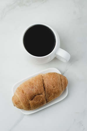 White mug with black coffee and croissant on white stone table. Top view. Coffee break.の写真素材