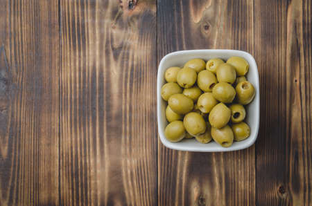 pickled green olives in a bowl on a wooden background. Top view, copyspace. Olives backgroundの写真素材