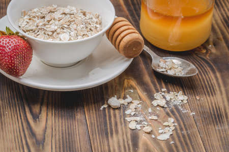 preparation of granule in a white bowl and honey dipper and strawberry on a wooden table.の写真素材