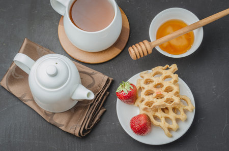Delicious breakfast with tea, honey and wafers decorated with fresh strawberry on a stone table. Top...