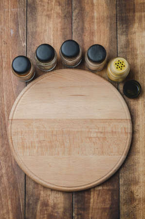 Various spices, round cutting board and cooking utensils on wooden table. Top viewの写真素材