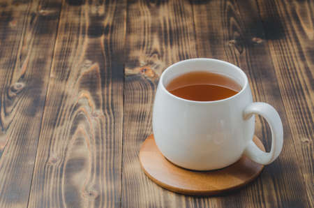 white cup with tea on a bamboo support on a wooden table, selective focus, copyspaceの写真素材